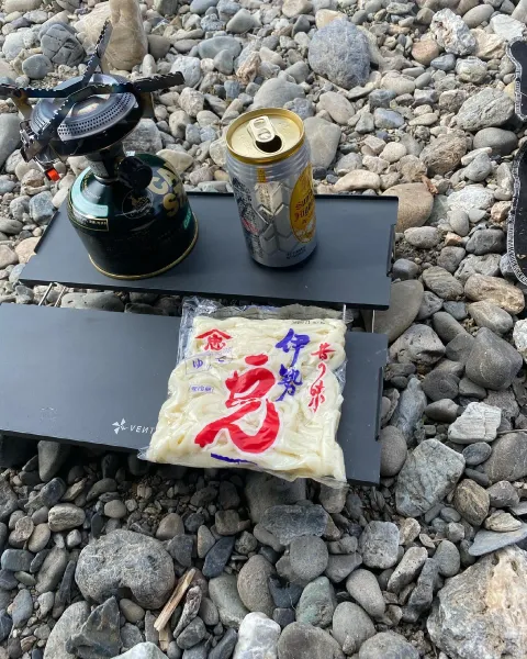 河原でのキャンプ調理。バーナーの脇に置いた伊勢うどんの袋