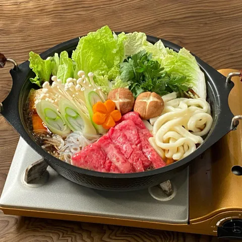 卓上鍋に牛肉と野菜、伊勢うどんを並べたすき焼き